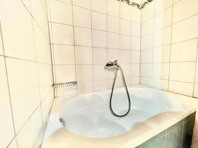 a bath tub with a shower in a white tiled bathroom at Nikolakis, Seafront- Harbor view in Symi