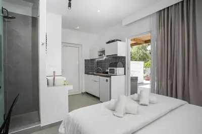 a white bedroom with a bed and a kitchen at Calma Luxury Studios & Suites in Faliraki