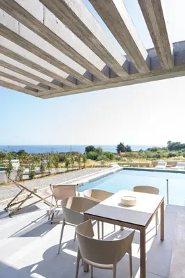 a patio with a table and chairs and a pool at Linear Cabanon Kallithea Luxury Villas in Koskinou