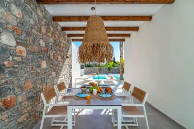 a dining room with a table and chairs and a stone wall at Villa Iviskus in Gennadi