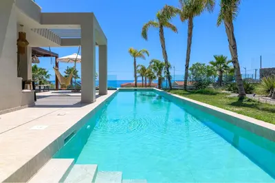 a swimming pool next to a house with palm trees at Villa Helios in Kiotari