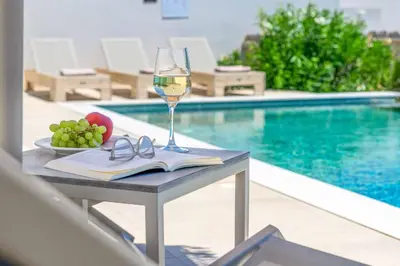 a glass of wine and a book on a table next to a pool at Massari Hills Villa 8 in Malona Village