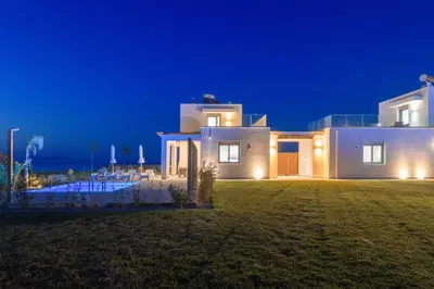 a large white house at night with the ocean at Villa Panaxia Keema in Theologos