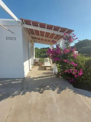 a porch of a white house with pink flowers at Charming Cottage on the sea turtle beach in Apolakkiá