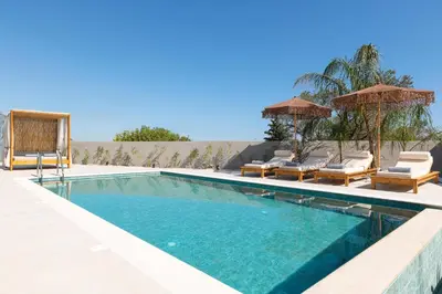 a swimming pool with chairs and umbrellas on a patio at Golf Beach Villa in Afantou
