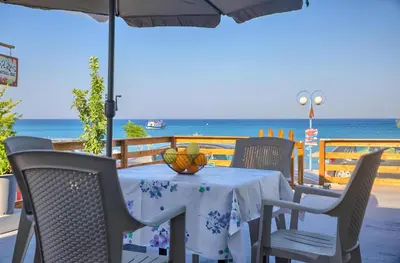 a table with chairs and an umbrella and the ocean at La mer stegna in Archangelos