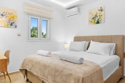 a bedroom with a bed with white walls and a window at Paul’s Garden Luxury House in Haraki