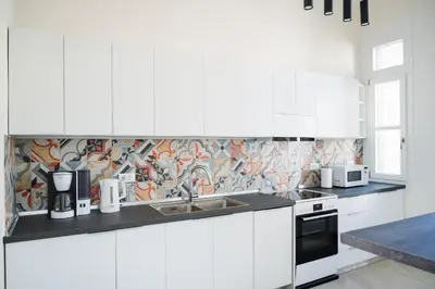 a kitchen with white cabinets and a tile wall at Alcestis City Apartment in Rhodes Town