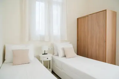 two beds in a white bedroom with a wooden cabinet at Alcestis City Apartment in Rhodes Town