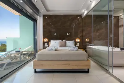 a bedroom with a large bed and a tub and a glass wall at Rhodes Skyline Suite with out Door Jacuzzi Sea View A2 in Ixia