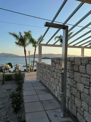 a stone wall next to the beach with palm trees at Sirin Luxury Suites Groundfloor in Haraki