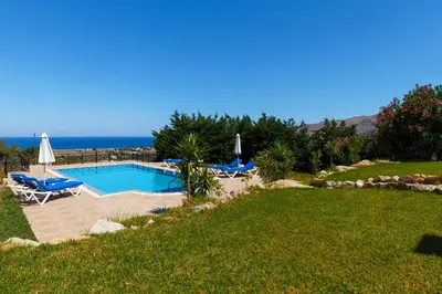 a swimming pool with chairs and the ocean in the background at Villa Alexi in Kalathos