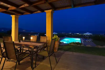 a dining table and chairs on a patio at night at Villa Alexi in Kalathos