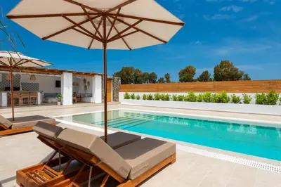 a swimming pool with an umbrella and lounge chairs and a swimming poolvisor at JOHANNES LUXURY VILLAS in Kolimbia
