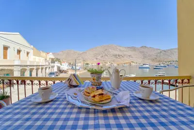 a table with a plate of food on top of a balcony at Waterfront House Pedi in Symi
