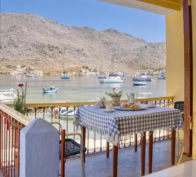 a table on a balcony with a view of a harbor at Waterfront House Pedi in Symi