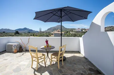a patio with a table and chairs and an umbrella at Traditional Greek Island Summer at Villa Julia in Kolimbia