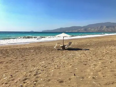 an umbrella and chairs on a beach with the ocean at Lovely independent room in Ecovilla on the beach in Apolakkiá