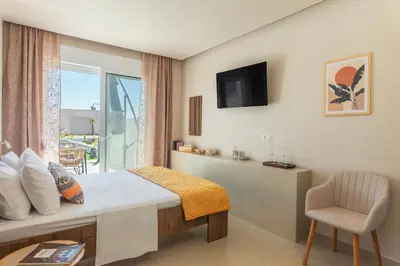 a bedroom with a bed with a window and a chair at Lago Beach Living in Faliraki
