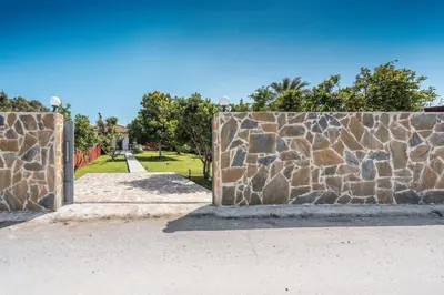 a stone wall next to a park with trees at Ily’s House in Pastida