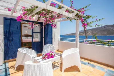 a patio with white chairs and a pergola with pink flowers at ILIDI Rock in Livadia