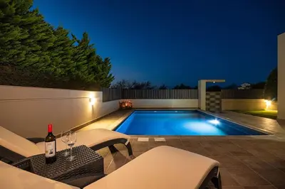 a swimming pool at night with a bottle of wine at Villa Serenity in Ialyssos