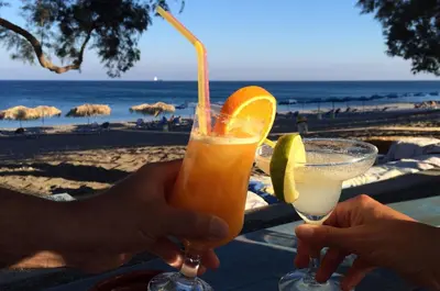 a person holding a drink in front of the beach at Almira Beach House in Kiotari