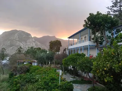 a blue building with trees and mountains in the background at Milios Studios in Megálon Choríon