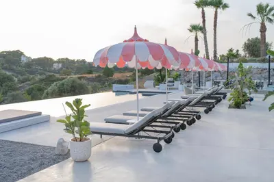 a row of lounge chairs under an umbrella on a pool at The Palms Concept Hotel Adults Only 16 Plus in Faliraki