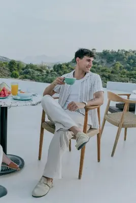 a young man sitting in a chair holding a cup at The Palms Concept Hotel Adults Only 16 Plus in Faliraki
