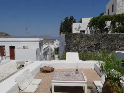 a patio with white chairs and a table and a wall at Lindos Traditional House in Rhodes Town