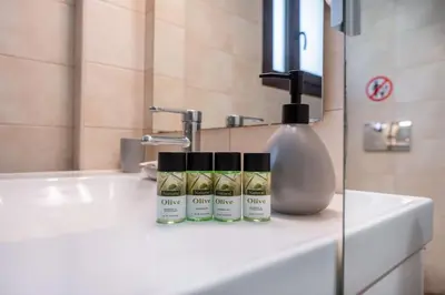 a bathroom sink with three products on it at Plumeria Alba Apartment in Rhodes Town