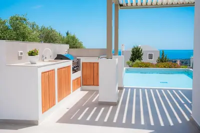 a patio with a kitchen and a swimming pool at Nostos Villa in Kalathos
