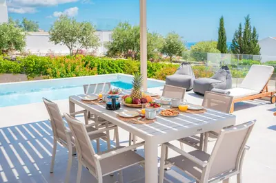 a white table and chairs on a patio with a pool at Nostos Villa in Kalathos