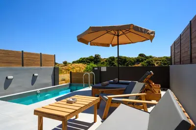 a patio with a table and an umbrella and a pool at ArmoniKon Pool Villas in Asgourou