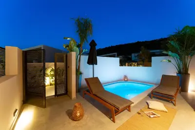 a patio with a pool and two chairs and a table at Afesou Suites in Ialyssos