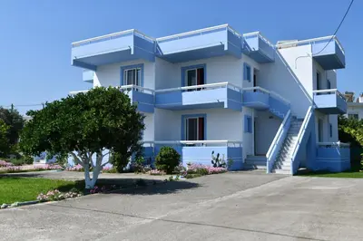 a white building with blue balconies and a tree at Blue Serenity Apartment 5 in Ialyssos