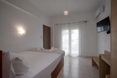 a white bedroom with a bed and a television at Stefanos House Stegna in Archangelos