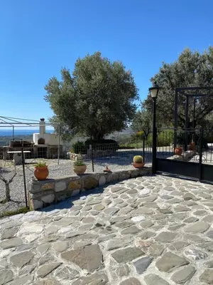 a stone patio with a black gate and a tree at Cullura in Asklipiḯon