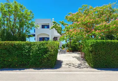 a white house with bushes in front of a building at Villa Costa Haraki in Haraki