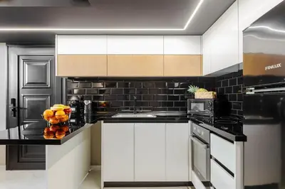 a kitchen with white cabinets and a black tile wall at Chrysma Urban Living in Rhodes Town