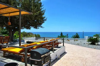 a group of lounge chairs on a patio with the beach at Alexandra's Sea Front Villa in Pefki Rhodes