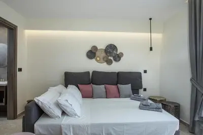 a white bed with pink pillows and a clock on the wall at Matsi Suites in Faliraki