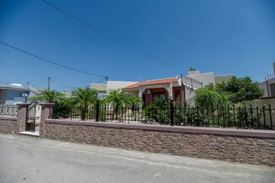 a house with a fence and palm trees on a street at Kira's Lovely Villa Massari in Haraki
