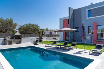 a swimming pool with chairs and umbrellas next to a building at Villa Pasadra in Afantou