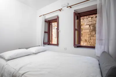 a white bedroom with a bed and two windows at Alexandras Stone House in Rhodes Town