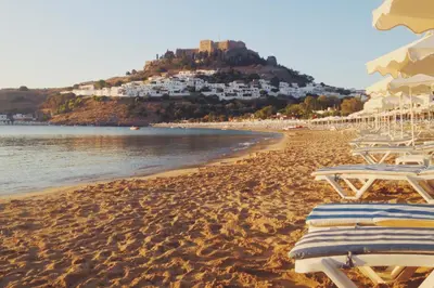 a beach with chaise lounges and umbrellas at Residenza Maria Lindos Villa in Líndos