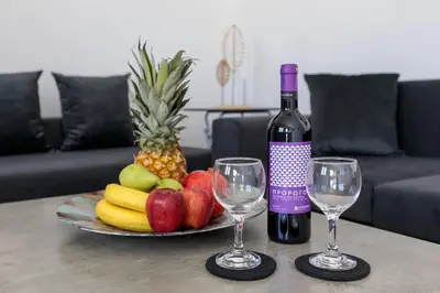a bottle of wine and two glasses on a table with fruit at Alamia Suites in Archangelos
