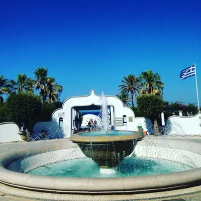 a water fountain in front of a building with palm trees at Golden Sand 2 in Ialyssos