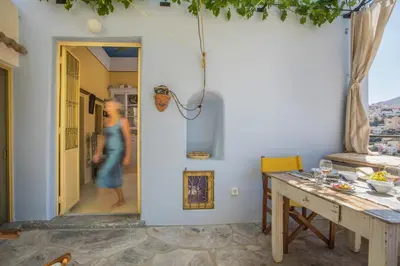a dining room with a table and a woman walking through the door at kalosymi house,Symi in Symi